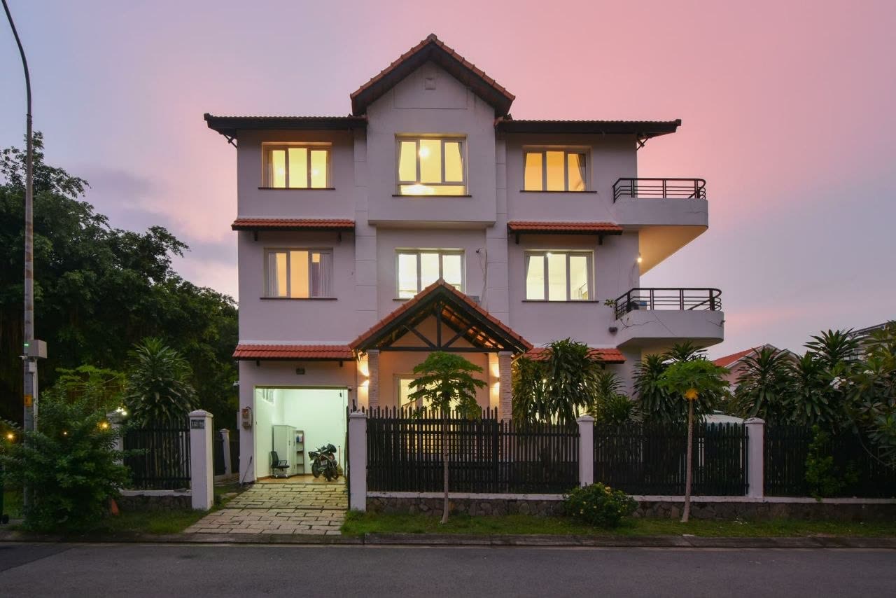 Villa 153 at dusk, three floors with warm light in every window, seen from the street