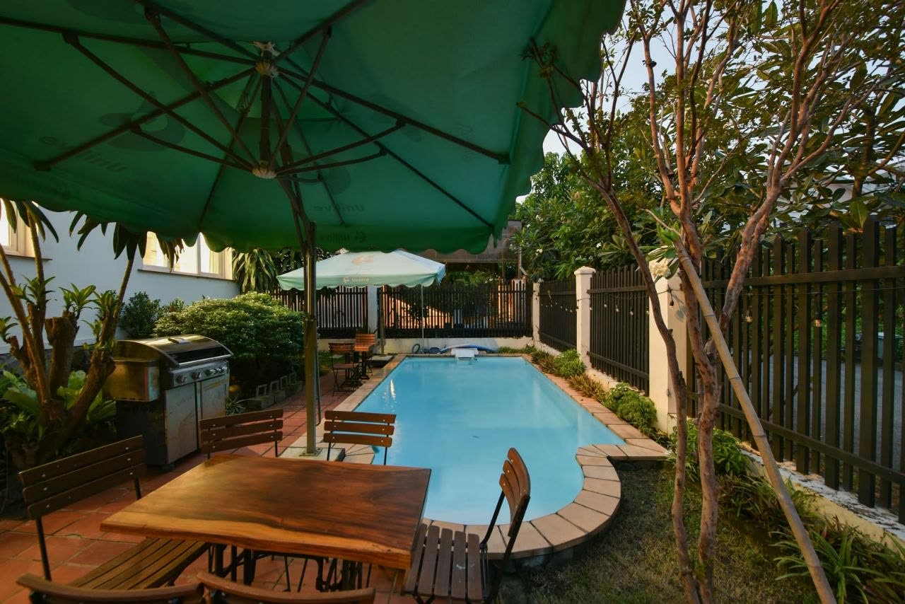 Private pool at dusk with outdoor dining table and BBQ under the trees