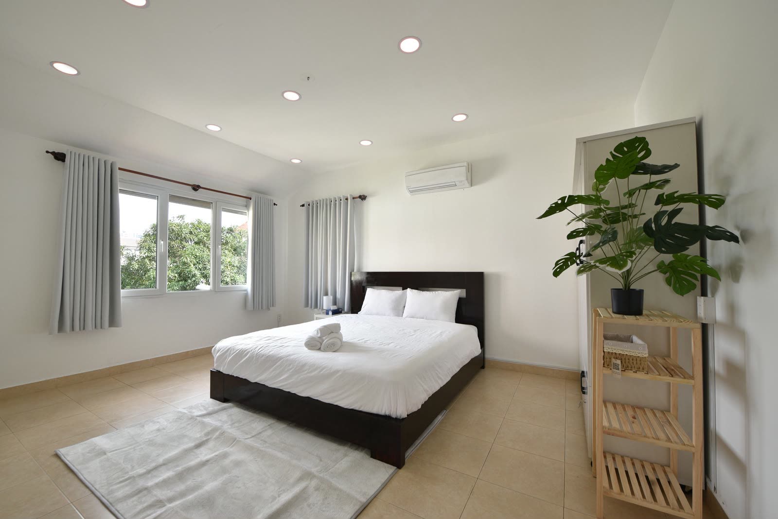 White bedroom with a queen bed, a plant and a wooden shelf