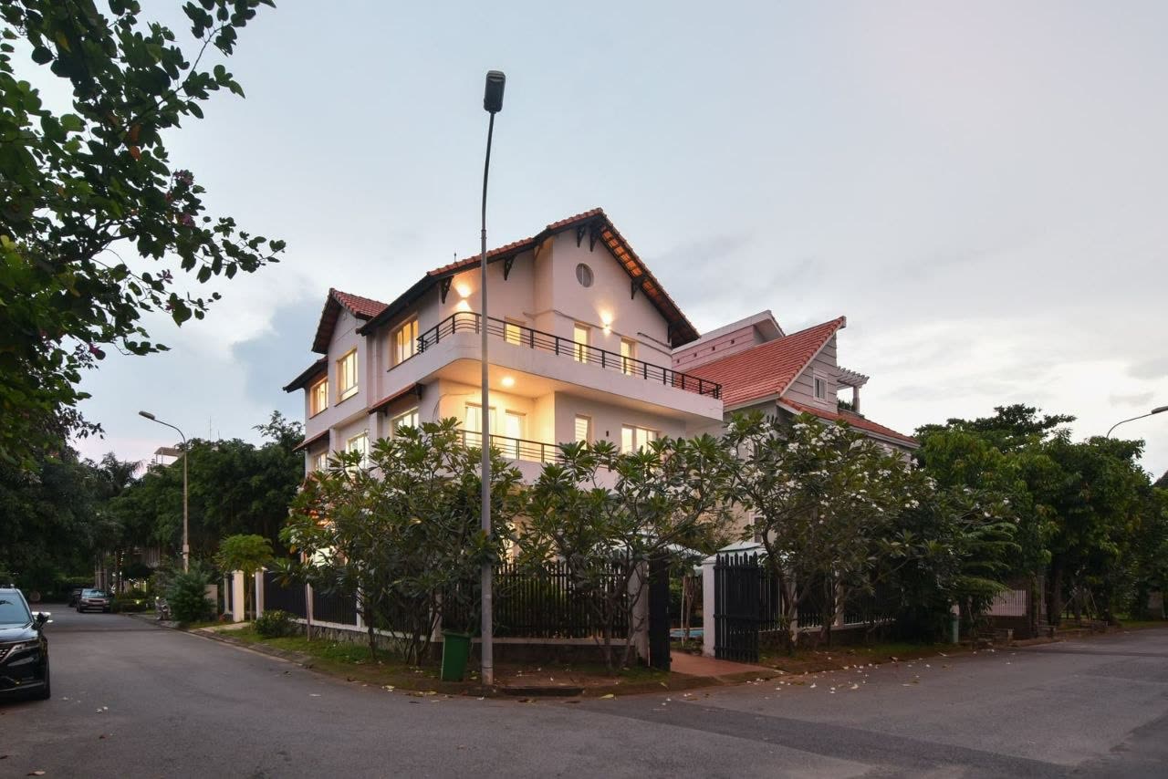 Villa 153 at dusk from the street corner, trees along the fence